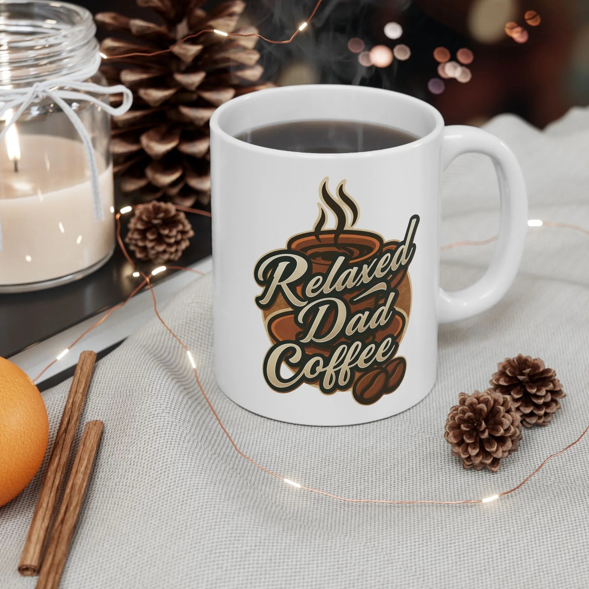 White coffee mug with "Relaxed Dad Coffee" text, surrounded by pine cones, cinnamon sticks, an orange, candle, and fairy lights